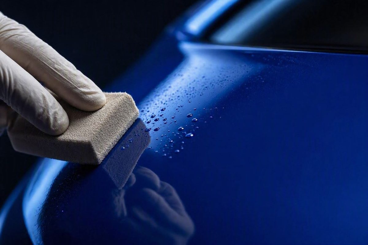 Suede applicator laying ceramic coating on dark blue paint with water beading